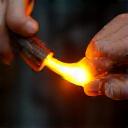 Close-up of an artisan wearing protective glasses, skillfully bending a glass tube over a fiery ribbon burner